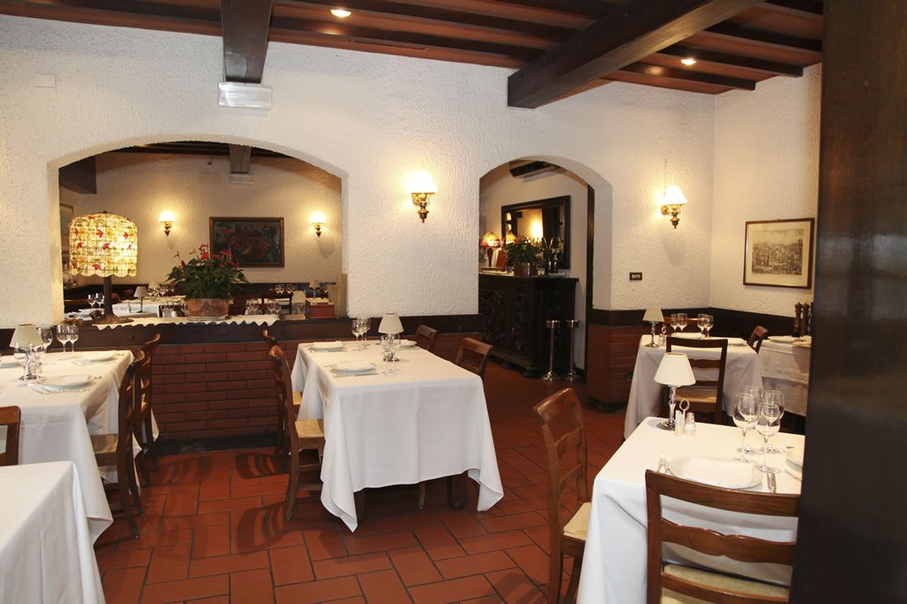 Sala della trattoria vista verso l'arco in mattoni, con tavoli apparecchiati e lampada Tiffany