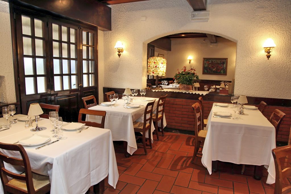 La sala principale della Trattoria Bianca: tavoli con tovaglie bianche, sedie in legno e muro di mattoni a vista sotto travi a soffitto